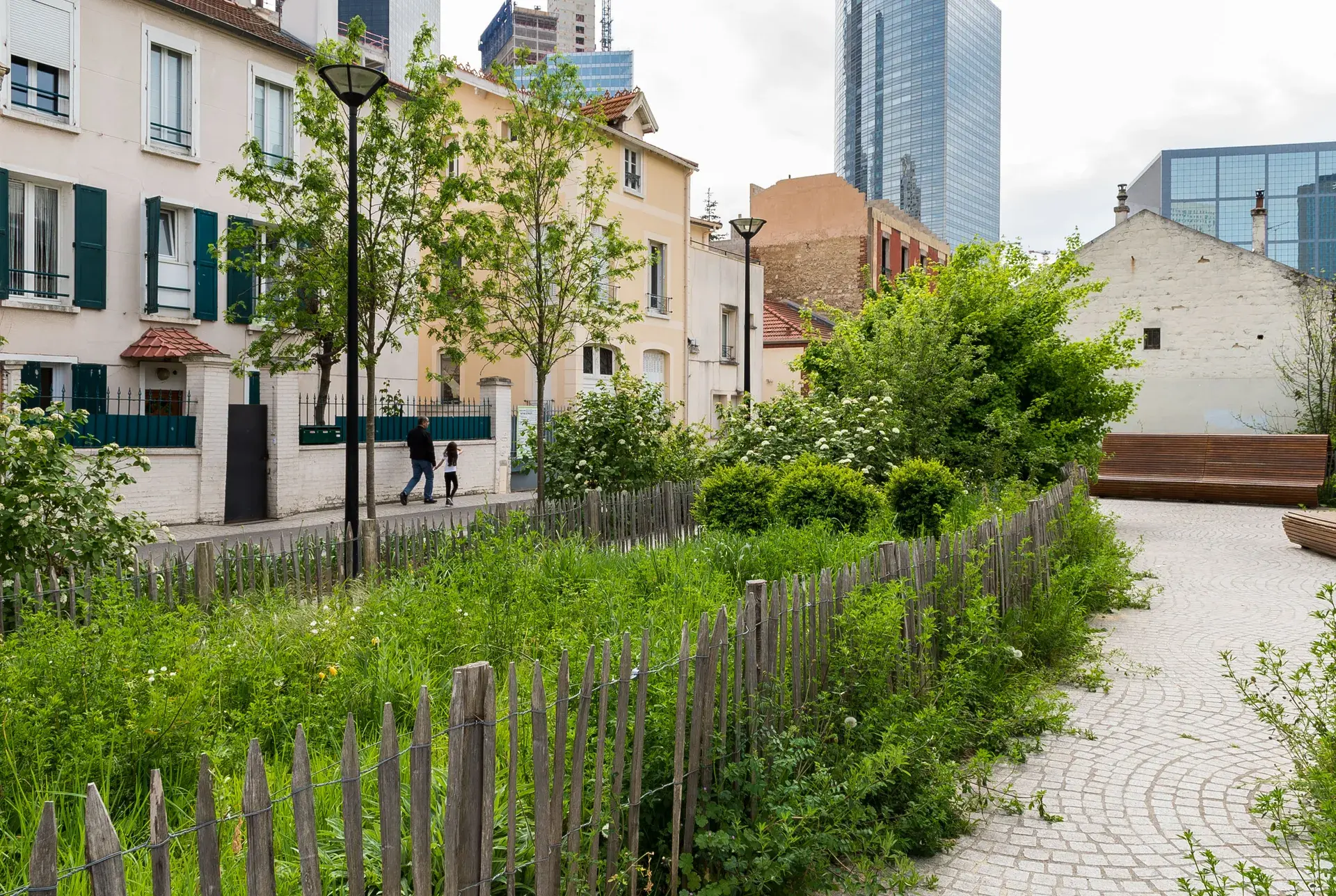 Jardin partagé clôturé devant maisons anciennes et tours de la Défense, quartier Marceau à Courbevoie