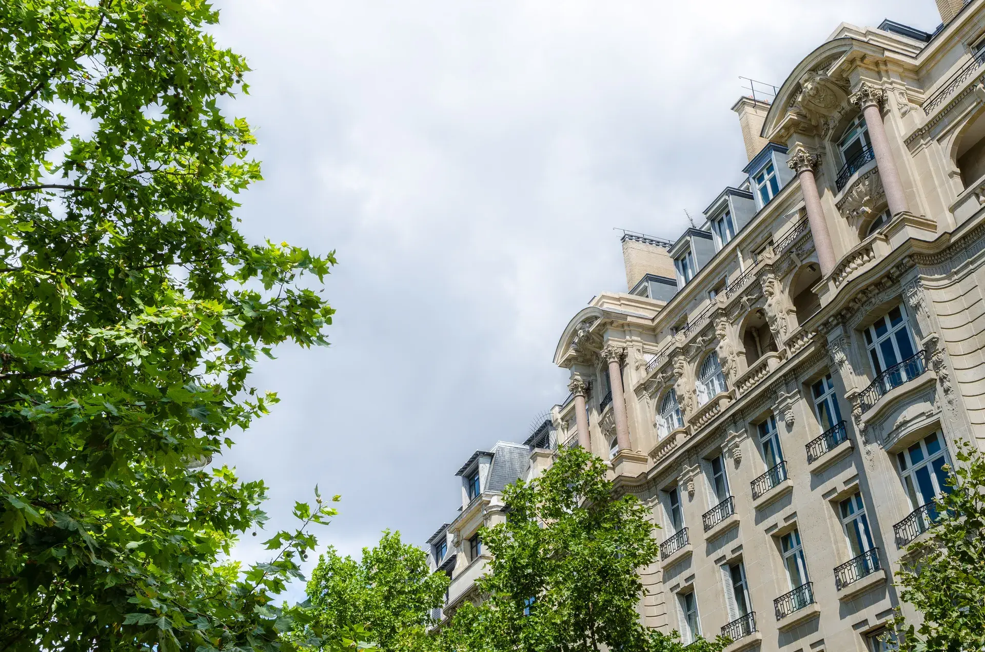 Façade d'immeuble haussmannien à colonnes vue depuis les arbres, Ternes-Maillot, Paris 17e