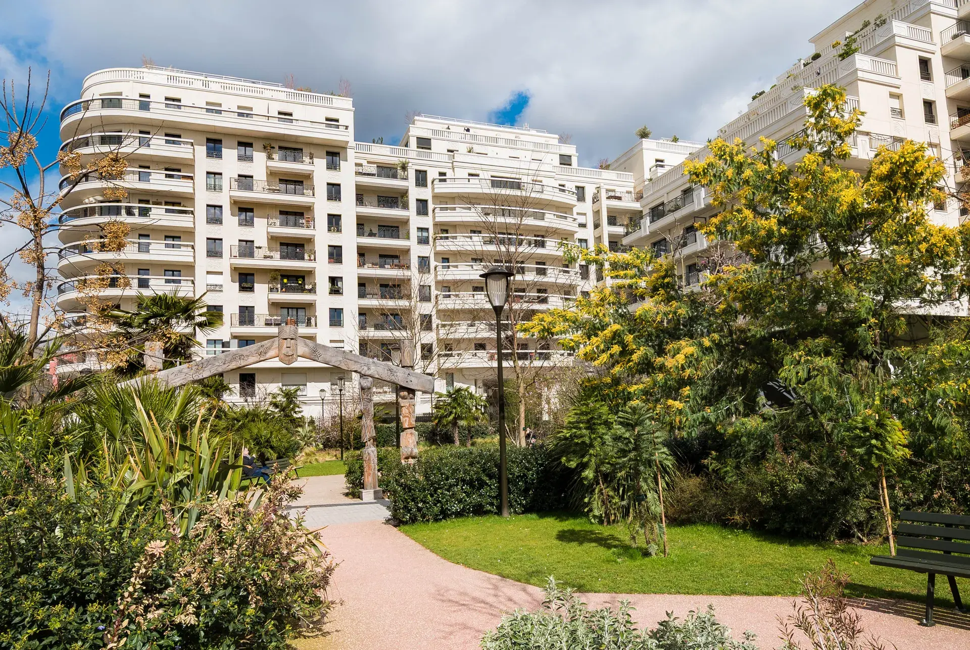 Jardin fleuri devant des résidences modernes blanches et un mimosa en fleurs, quartier Collange à Levallois-Perret