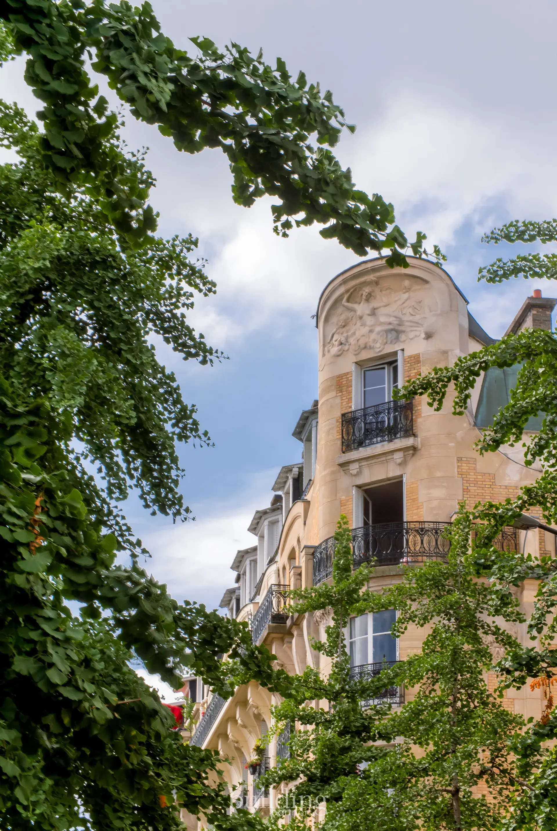 Tourelle d'angle d'un immeuble ancien sculpté entouré de feuillages, quartier Jean-Zay à Levallois-Perret
