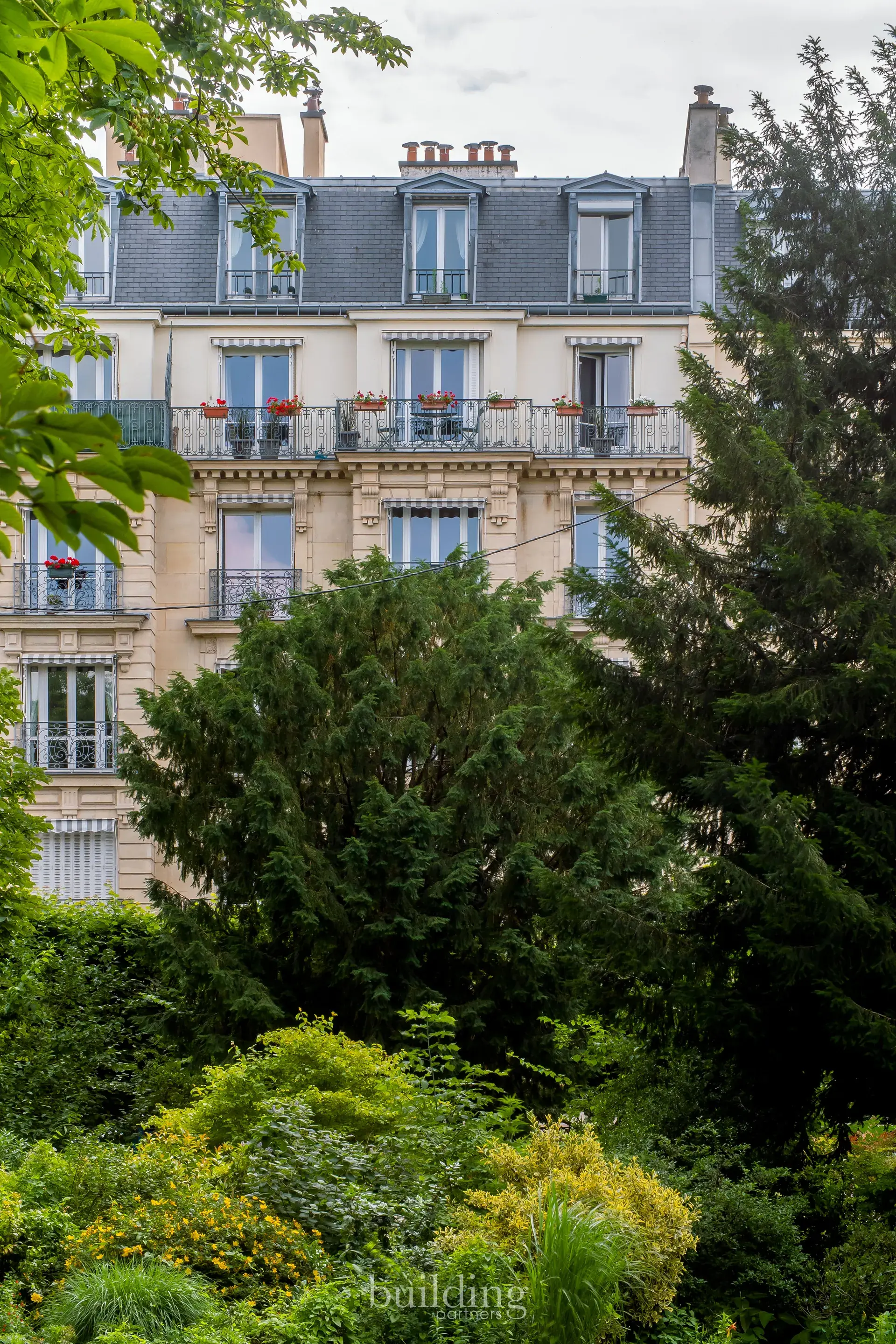 Immeuble ancien à toiture d'ardoise vu à travers les arbres du parc, quartier Planchette à Levallois-Perret