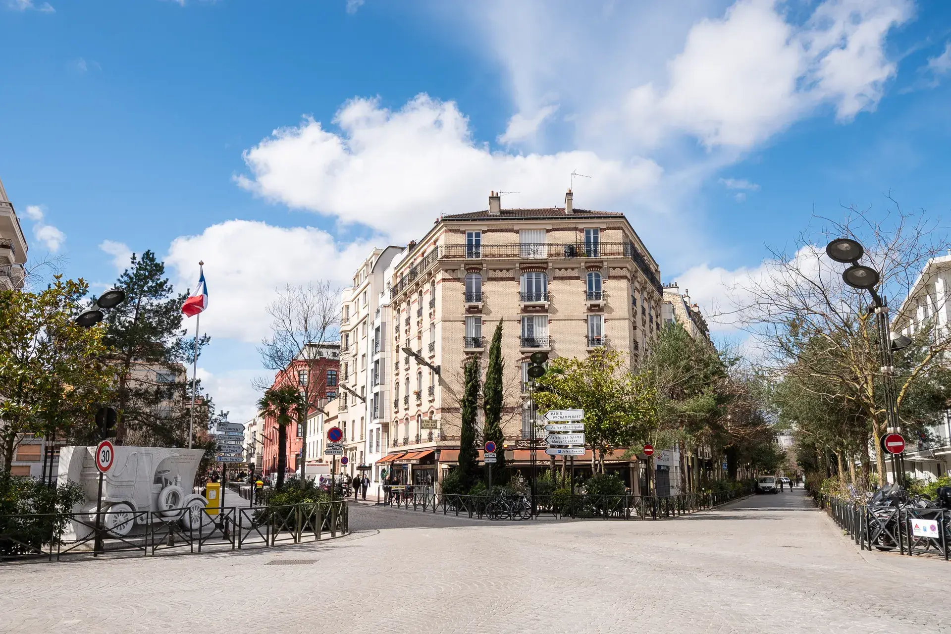Place pavée avec immeuble haussmannien d'angle et drapeaux tricolores, quartier Collange à Levallois-Perret