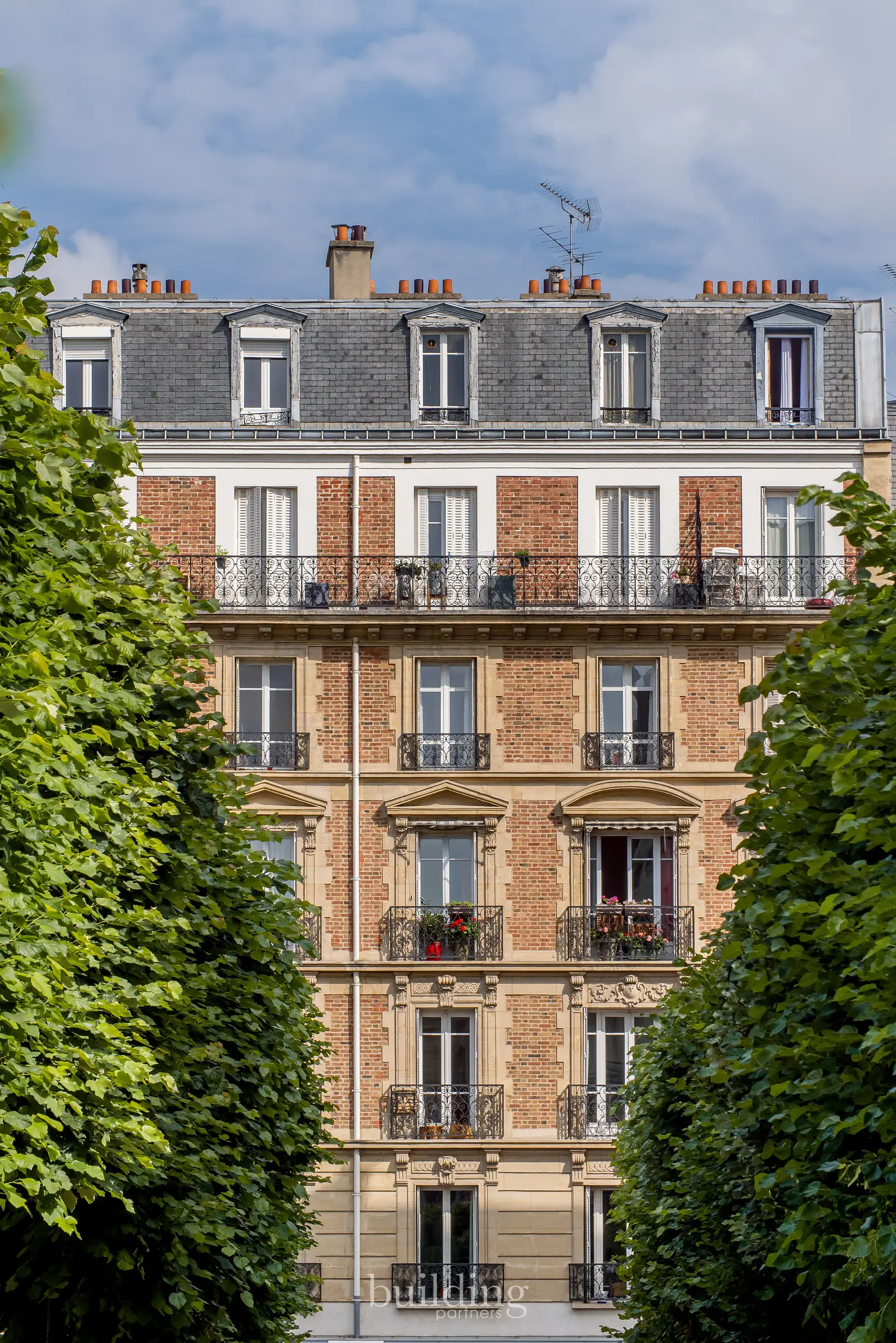 Façade en brique d'un immeuble ancien encadrée par des arbres taillés, quartier Mairie à Levallois-Perret