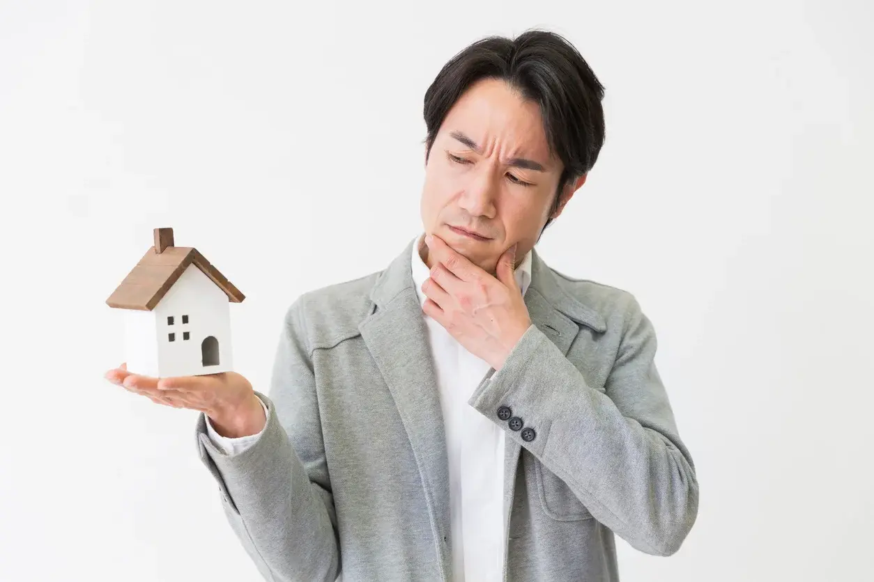 Photo d'un homme se questionnant et tenant une maison miniature. Utilisée dans l'article sur le mandat immobilier simple ou exclusif de Building Partners.Crédits : miya227. Référence de la photo : 1126580973.