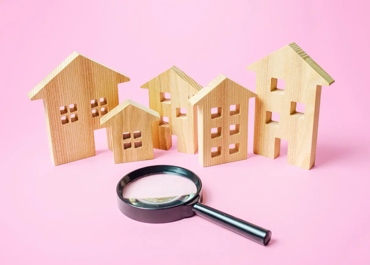 Photo de jouets en bois en forme de maisons et d'une loupe, avec un fond rose clair. Utilisée dans l'article Building Partners sur l'état du marché immobilier2026 d'après les derniers chiffres DVF. Crédits iStock : Andrii Yalanskyi. Référence : 1276627933